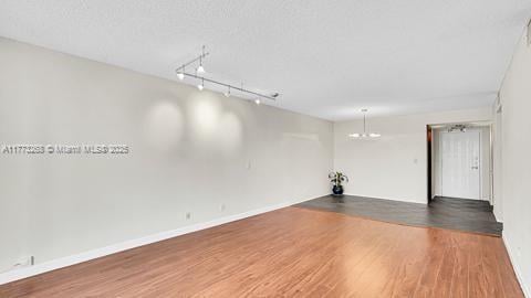 unfurnished room with baseboards, wood finished floors, and a chandelier