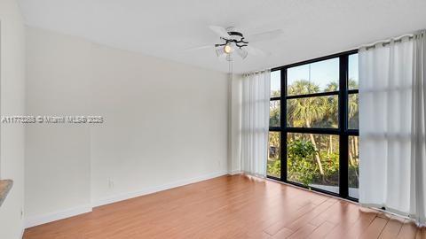 empty room with wood finished floors, a ceiling fan, expansive windows, and a wealth of natural light