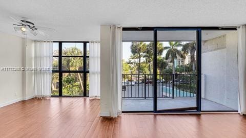doorway with baseboards, ceiling fan, a wall of windows, and wood finished floors