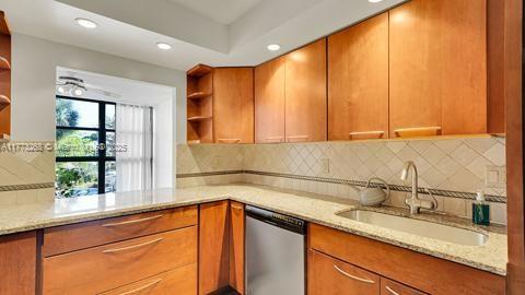 kitchen with tasteful backsplash, stainless steel dishwasher, open shelves, a sink, and light stone counters