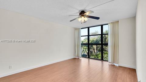 spare room featuring expansive windows, baseboards, ceiling fan, and wood finished floors