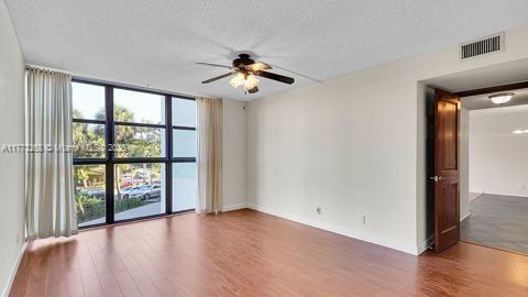 empty room featuring a wall of windows, a ceiling fan, visible vents, wood finished floors, and baseboards