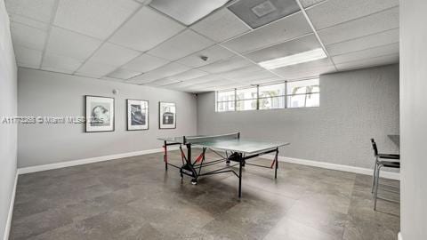 game room with concrete flooring, baseboards, and a drop ceiling