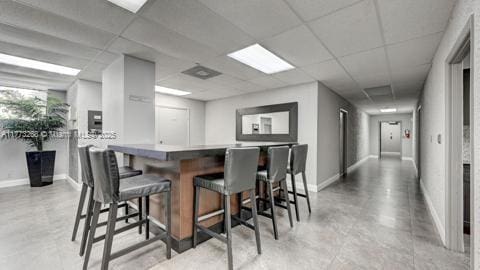 bar featuring baseboards, a community bar, concrete flooring, and a paneled ceiling