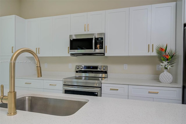 kitchen featuring appliances with stainless steel finishes, a sink, white cabinets, and light stone countertops