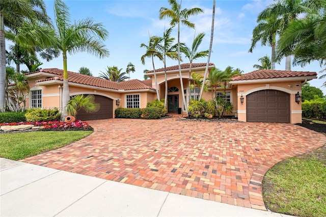 mediterranean / spanish-style house featuring a tiled roof, decorative driveway, stucco siding, and an attached garage