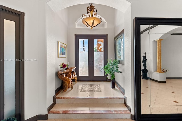 tiled foyer featuring baseboards, decorative columns, arched walkways, and french doors