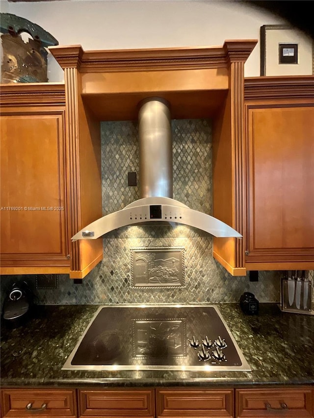 interior space featuring wall chimney range hood, brown cabinets, black electric cooktop, and decorative backsplash