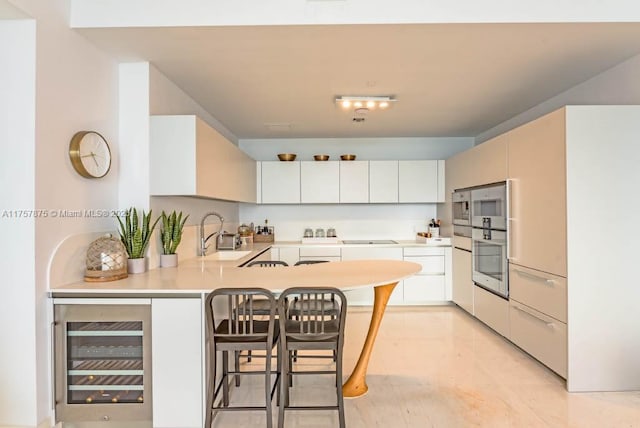 16901 Collins Ave Unit 1404, Sunny Isles Beach, FL 33160 - kitchen with beverage cooler, a peninsula, light countertops, a breakfast bar area, and stainless steel double oven