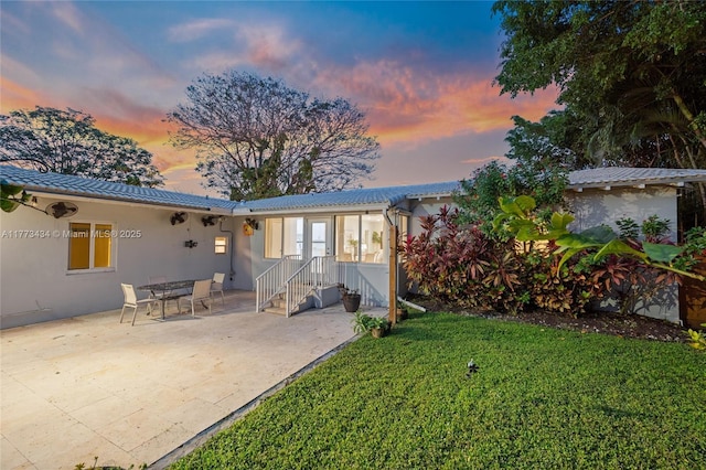 74 NE 103rd St, Miami Shores, FL 33138 - back of house at dusk featuring a yard, stucco siding, and a patio area