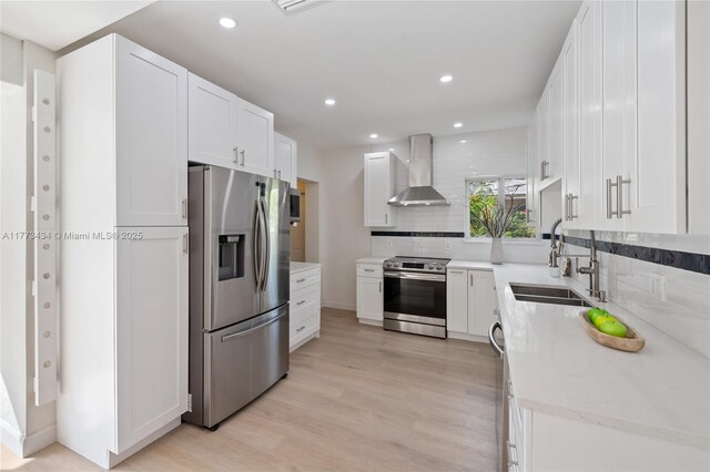 74 NE 103rd St, Miami Shores, FL 33138 - kitchen featuring stainless steel appliances, wall chimney exhaust hood, a sink, tasteful backsplash, and light wood-style flooring