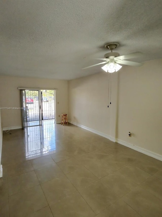 spare room with a textured ceiling, light tile patterned floors, baseboards, and a ceiling fan