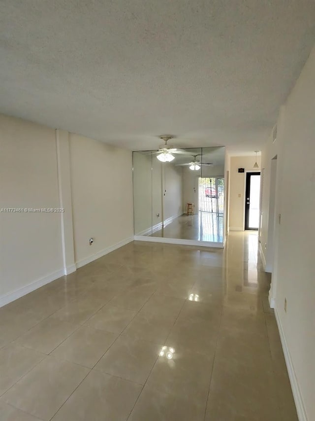 unfurnished room with light tile patterned flooring, a textured ceiling, baseboards, and a ceiling fan