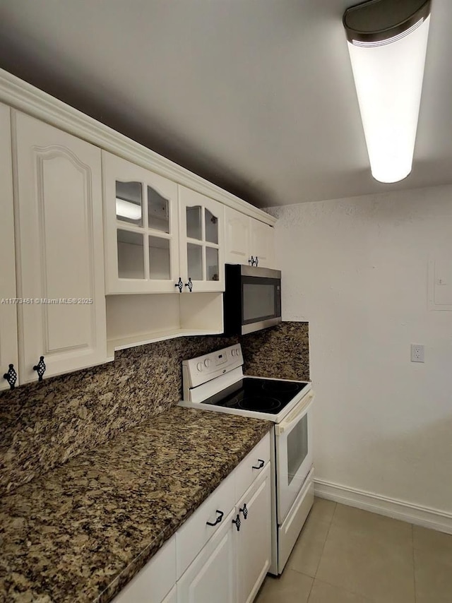 kitchen featuring stainless steel microwave, decorative backsplash, electric stove, light tile patterned flooring, and glass insert cabinets