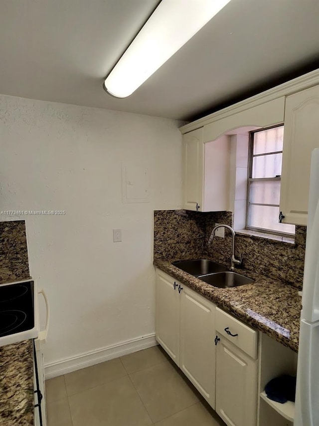 kitchen with light tile patterned flooring, a sink, freestanding refrigerator, white cabinets, and decorative backsplash
