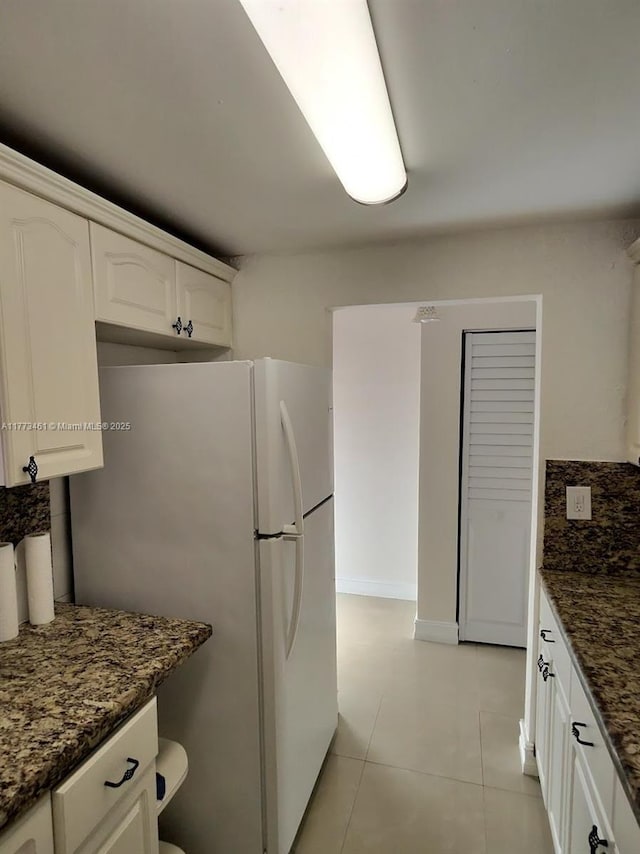 kitchen featuring light tile patterned flooring, decorative backsplash, dark stone counters, white cabinetry, and freestanding refrigerator
