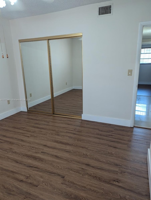 unfurnished bedroom featuring a closet, baseboards, dark wood-style floors, and visible vents
