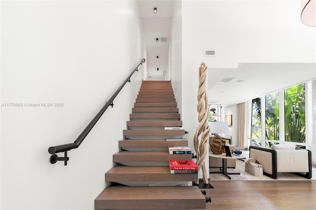 stairs featuring visible vents, wood finished floors, a wall of windows, and a towering ceiling