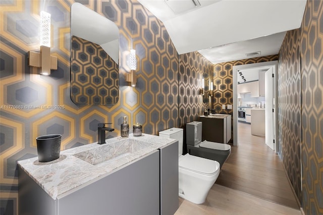 bathroom with visible vents, wallpapered walls, and wood finished floors