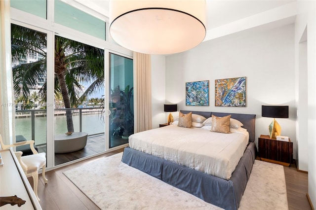 bedroom featuring access to exterior, a water view, and wood finished floors