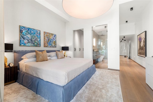 bedroom with a towering ceiling, wood finished floors, and ensuite bathroom