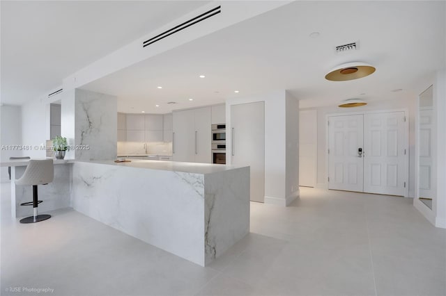 3201 S Ocean Blvd Unit 704, Highland Beach, FL 33487 - kitchen featuring modern cabinets, a peninsula, stainless steel double oven, light stone counters, and a breakfast bar area