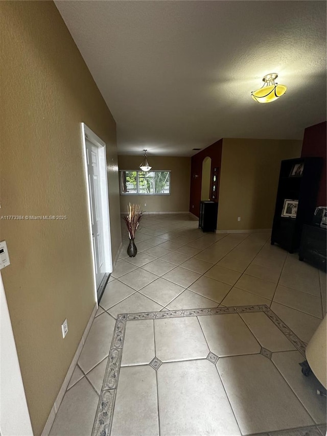 hall featuring baseboards, a textured wall, and light tile patterned floors
