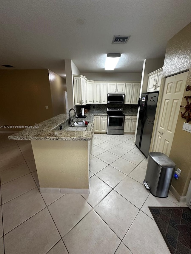 kitchen with a sink, stone countertops, appliances with stainless steel finishes, a peninsula, and light tile patterned floors
