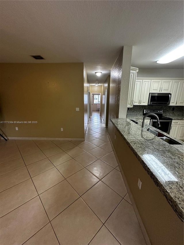 kitchen featuring decorative backsplash, white cabinets, appliances with stainless steel finishes, a sink, and light tile patterned floors