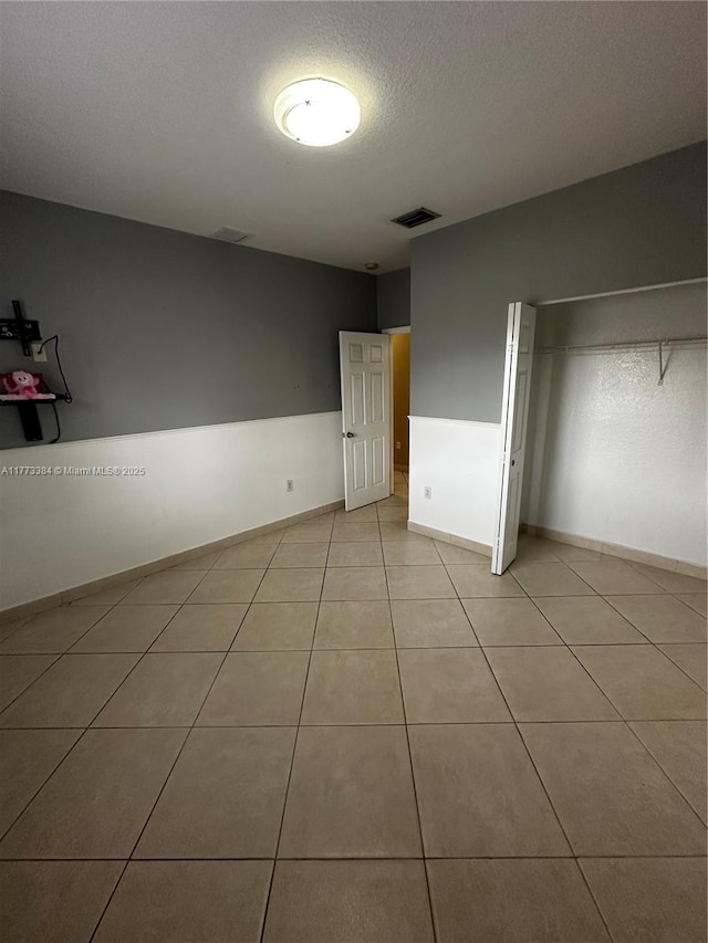 unfurnished bedroom featuring baseboards, a textured ceiling, visible vents, and light tile patterned floors