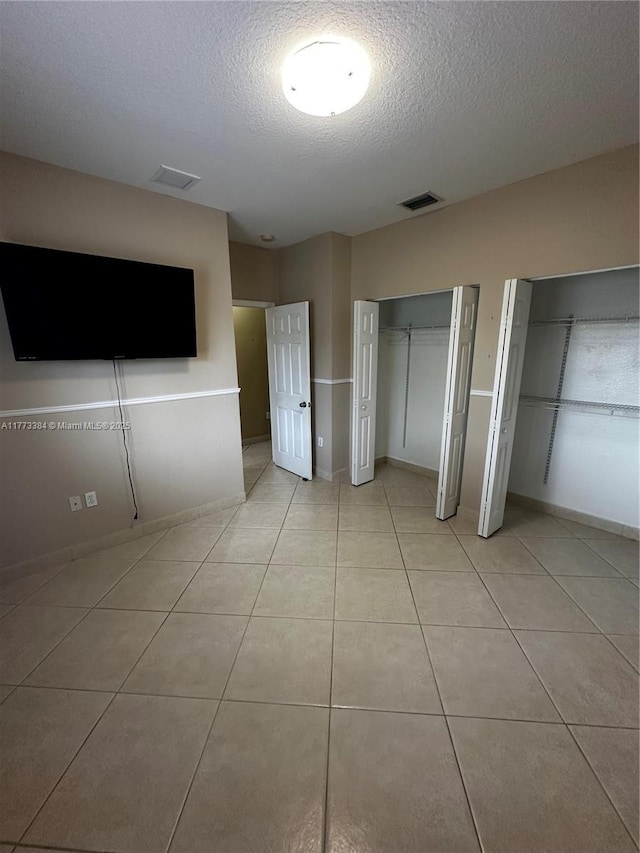 unfurnished bedroom featuring light tile patterned flooring, visible vents, multiple closets, and a textured ceiling
