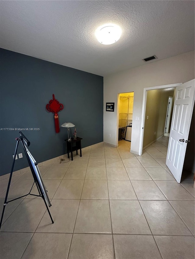 unfurnished bedroom featuring a textured ceiling, visible vents, baseboards, and light tile patterned floors