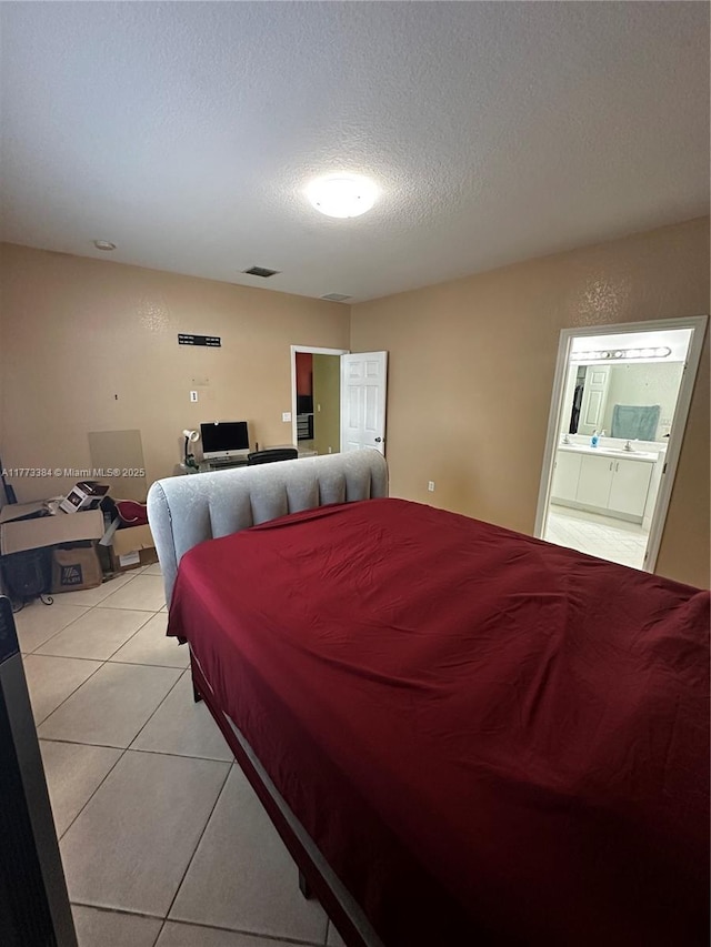 bedroom featuring ensuite bathroom, visible vents, light tile patterned floors, and a textured ceiling