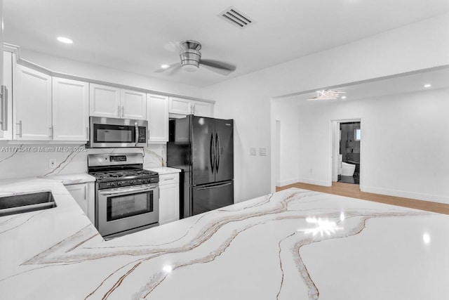 kitchen featuring appliances with stainless steel finishes, white cabinets, light stone countertops, and visible vents