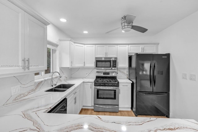 kitchen with light stone countertops, ceiling fan, a sink, white cabinetry, and black appliances
