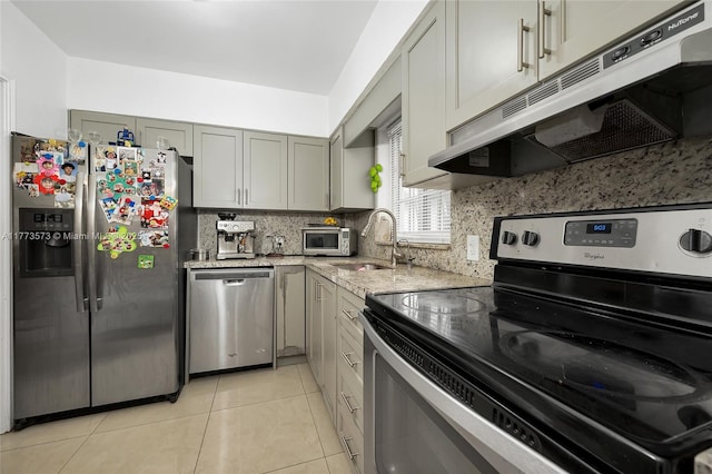 kitchen featuring light tile patterned flooring, light stone counters, backsplash, a sink, and stainless steel appliances