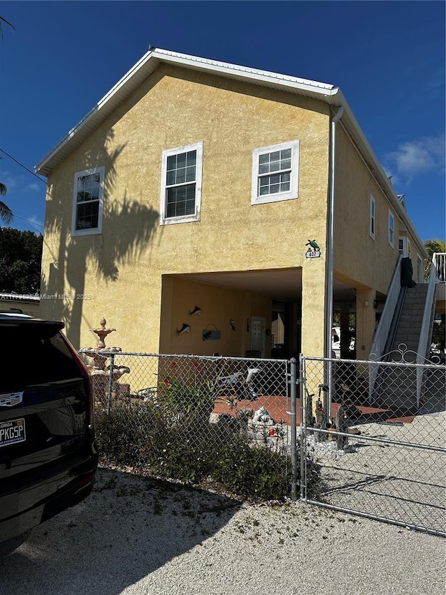 rear view of property with stucco siding, stairs, and a fenced front yard