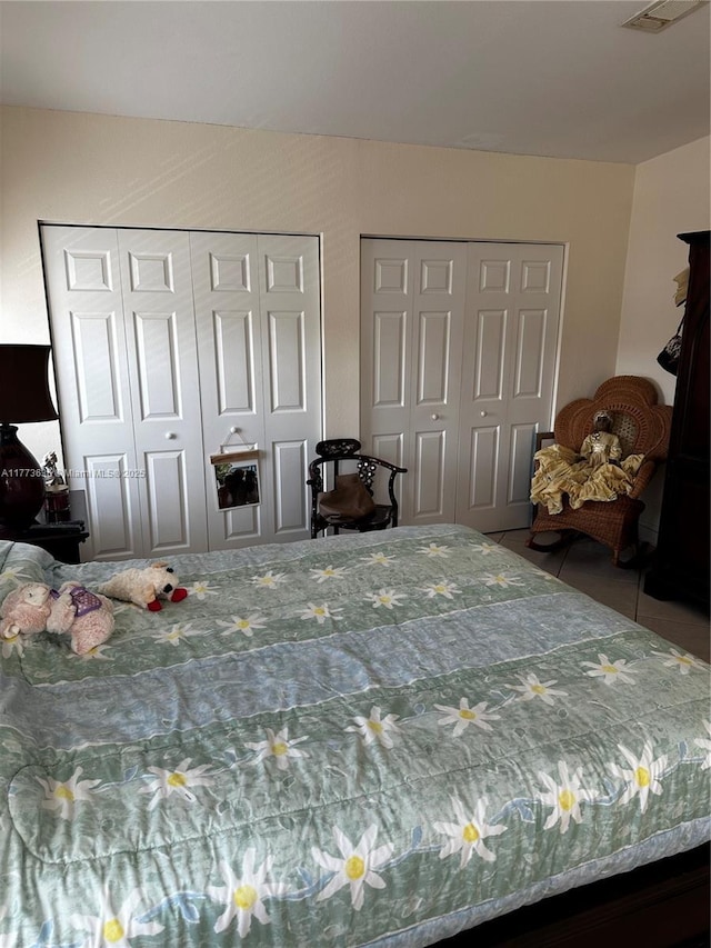 bedroom featuring two closets, tile patterned floors, and visible vents
