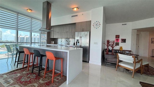 3131 NE 188th St Unit 2-1002, Aventura, FL 33180 - kitchen with stainless steel refrigerator with ice dispenser, island exhaust hood, decorative backsplash, a kitchen island, and a kitchen bar