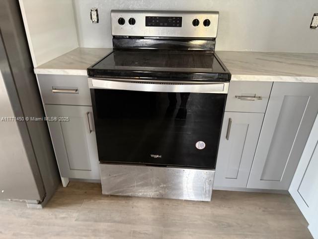 kitchen with gray cabinets, light wood-style floors, stainless steel appliances, and light stone counters