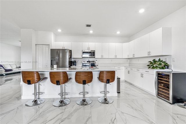 kitchen with a kitchen bar, appliances with stainless steel finishes, light countertops, beverage cooler, and marble finish floor