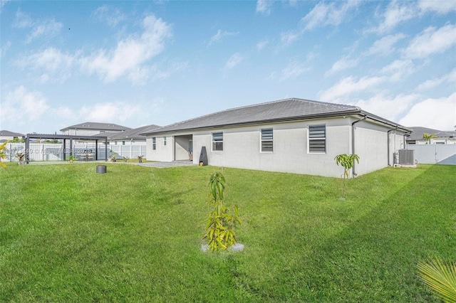 back of house with a lawn, central AC unit, a fenced backyard, and stucco siding