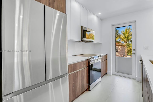 kitchen with light countertops, light tile patterned flooring, white cabinets, modern cabinets, and appliances with stainless steel finishes
