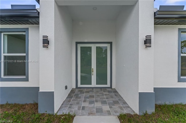 view of exterior entry with french doors, stucco siding, and metal roof
