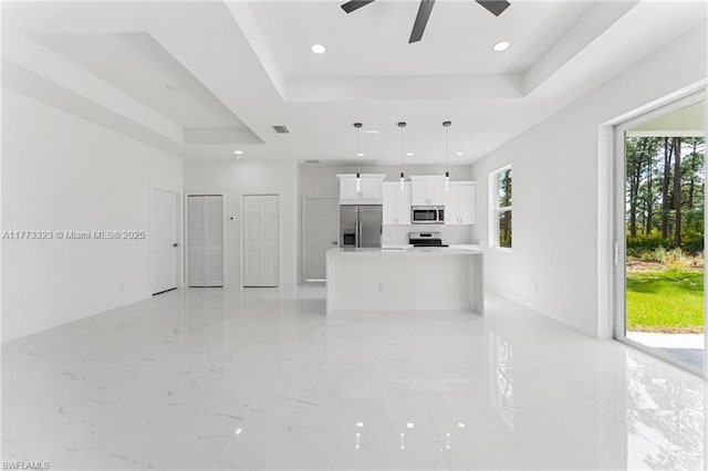 unfurnished living room with a tray ceiling, a ceiling fan, marble finish floor, visible vents, and recessed lighting