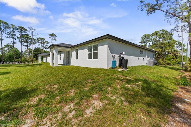 back of house with cooling unit, stucco siding, and a lawn