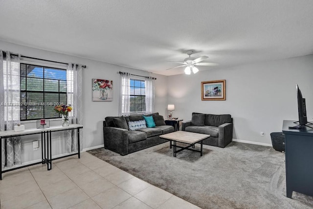 living room with a textured ceiling, baseboards, ceiling fan, light carpet, and light tile patterned floors