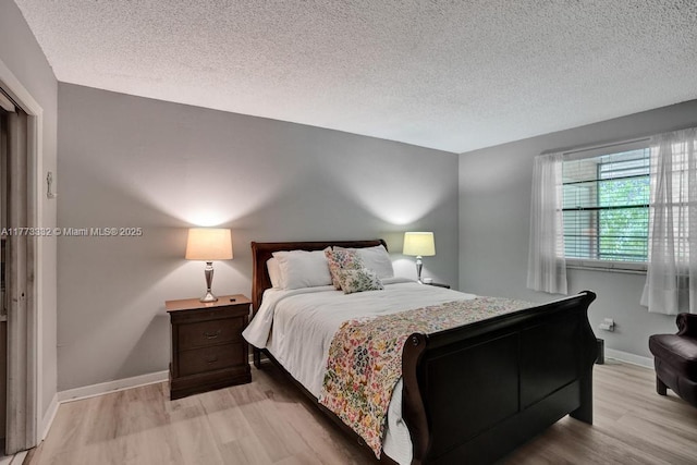 bedroom featuring a textured ceiling, baseboards, and light wood-type flooring