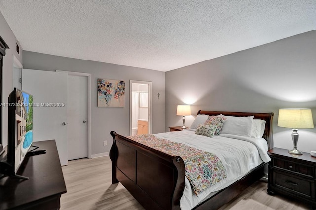 bedroom featuring connected bathroom, visible vents, light wood-style floors, and a textured ceiling