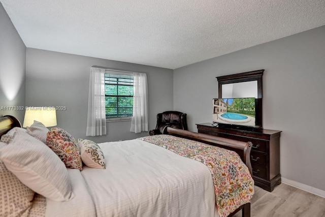 bedroom with baseboards, light wood finished floors, and a textured ceiling